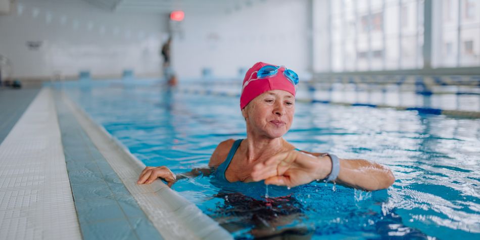 Senior woman looking at smartwatch when swimming in indoors swimming pool